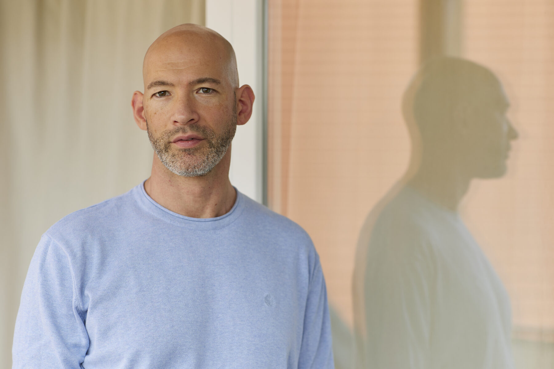 Porträtaufnahme von vorne: Hannes Lerchbacher, Psychotherapeut in Ausbildung unter Supervision, steht vor einer reflektierenden Glasfront und blickt gerade in die Kamera.