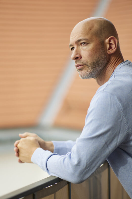 Porträtaufnahme von der linken Seite: Hannes Lerchbacher, Psychotherapeut in Ausbildung unter Supervision, lehnt an einem Geländer und blickt an der Kamera vorbei.